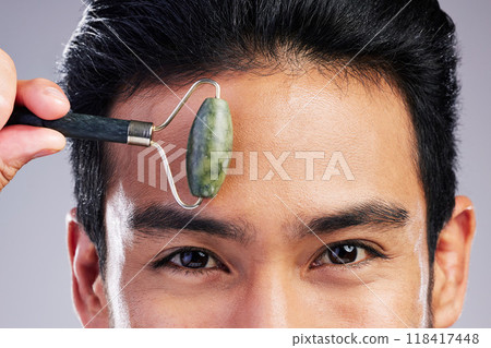 Man, portrait or face massage with roller or quartz product for healthy skincare on studio background. Forehead, crystal stone treatment or male model with facial dermatology cosmetic for beauty glow Man, portrait or face massage with roller or quartz product for healthy skincare on studio background. Forehead, crystal stone treatment or male model with facial dermatology cosmetic for beauty glow 118417448