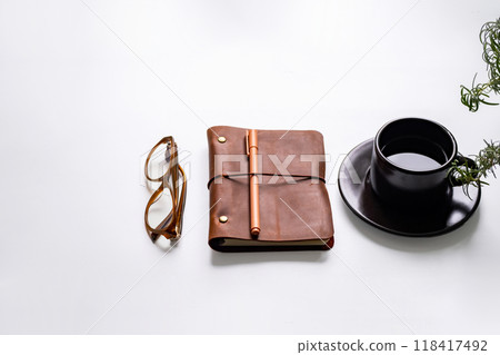 Office essentials with coffee cup, glasses, notebook and plant on white desk. Office essentials with coffee cup, glasses, notebook and plant on white desk. 118417492