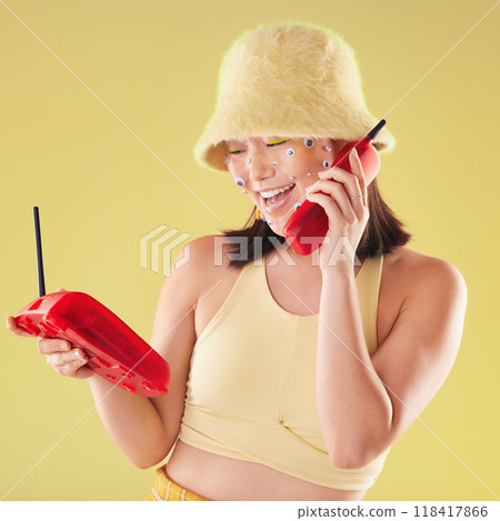Woman, landline phone call and studio background for yellow fashion, excited and smile with eyes sticker art on face. Asian gen z model, 90s aesthetic and telephone communication, talk or happy chat 118417866