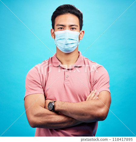 Man in face mask, arms crossed in portrait and covid, safety from virus, bacteria and germs isolated on blue background. Disease, corona and male person, health compliance with protection in studio 118417895