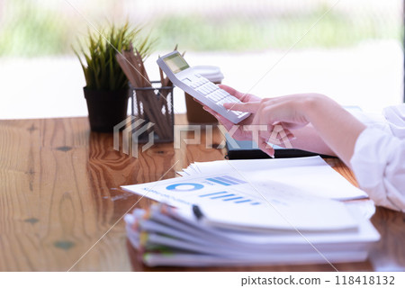 Hand of a businesswoman working with a calculator and documents at a desk in the office. Hand of a businesswoman working with a calculator and documents at a desk in the office. 118418132