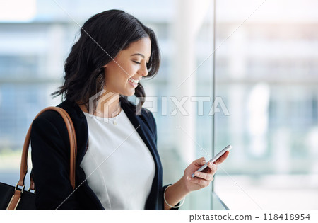 Her teams reporting good news today. Cropped shot of an attractive young businesswoman using a smartphone while standing in a modern office. 118418954