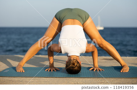On windy day young slender woman does yoga near sea doing practicing hatha yoga 118419356