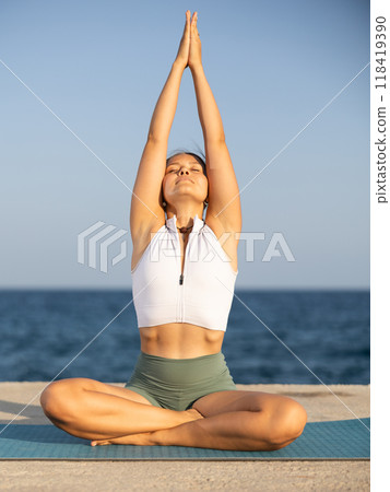 Athletic girl practicing lotus pose of yoga on seashore Athletic girl practicing lotus pose of yoga on seashore 118419390