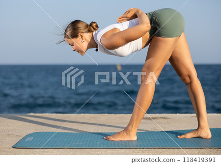 On windy day young slender woman does yoga near sea doing Parshvottanasana On windy day young slender woman does yoga near sea doing Parshvottanasana 118419391