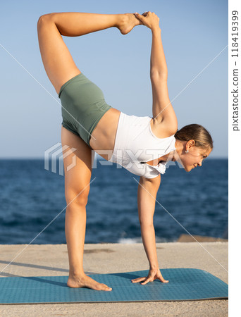 Sportive girl practicing half moon pose of yoga on seashore Sportive girl practicing half moon pose of yoga on seashore 118419399