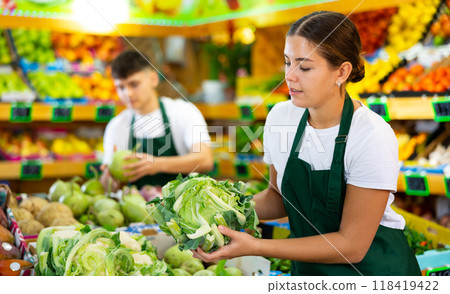 Supermarket female employee lays out cauliflower on shelves in greengrocery store 118419422