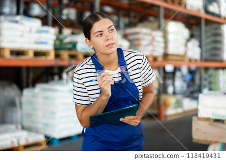 In warehouse of store, girl checks quantity of goods and receipt documents for products In warehouse of store, girl checks quantity of goods and receipt documents for products 118419431
