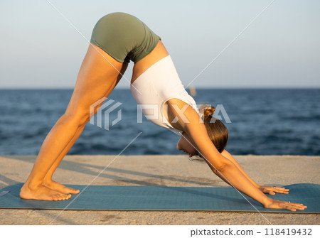 On windy day young slender woman does yoga near sea doing Adho Mukha Svanasana On windy day young slender woman does yoga near sea doing Adho Mukha Svanasana 118419432
