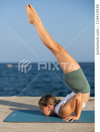 Sportive girl practicing chest stand pose of yoga on seashore 118419436