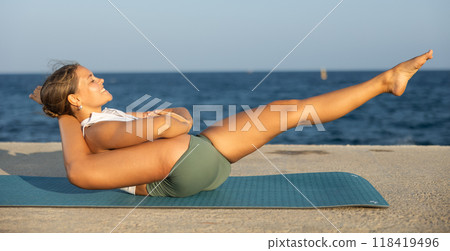 On windy day young slender woman does yoga near sea doing yoganidrasan 118419496