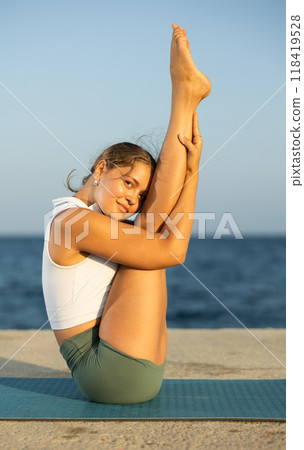 Sportive girl practicing boat pose of yoga on seashore Sportive girl practicing boat pose of yoga on seashore 118419528