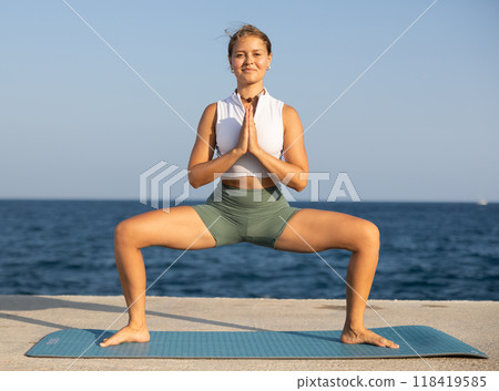Sportive girl practicing frog pose of yoga on seashore Sportive girl practicing frog pose of yoga on seashore 118419585