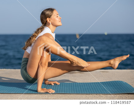On windy day young slender woman does yoga near sea doing titibasana On windy day young slender woman does yoga near sea doing titibasana 118419587