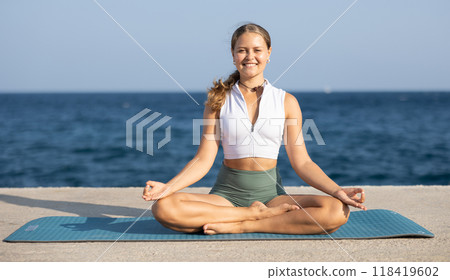 On windy day young slender woman does yoga near sea doing padmasana On windy day young slender woman does yoga near sea doing padmasana 118419602