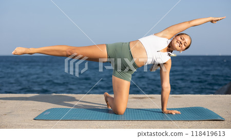 Sportive girl practicing kneeling half moon pose of yoga on seashore 118419613