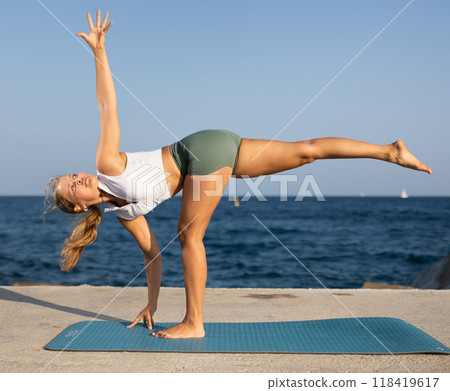 Athletic girl meditates in a yoga pose parshvottanasana on seashore 118419617