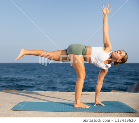 Athletic girl meditates in a yoga pose parshvottanasana on seashore 118419620