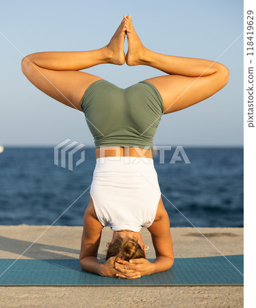 On windy day young slender woman does yoga near sea doing shirshasana On windy day young slender woman does yoga near sea doing shirshasana 118419629