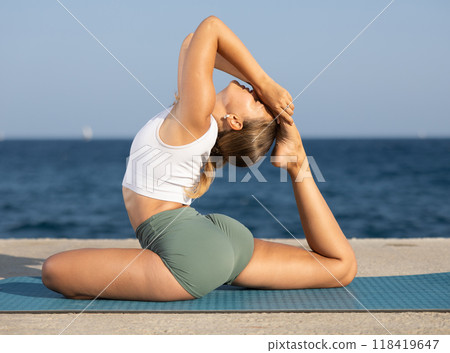 Sportive girl practicing king pigeon pose of yoga on seashore Sportive girl practicing king pigeon pose of yoga on seashore 118419647