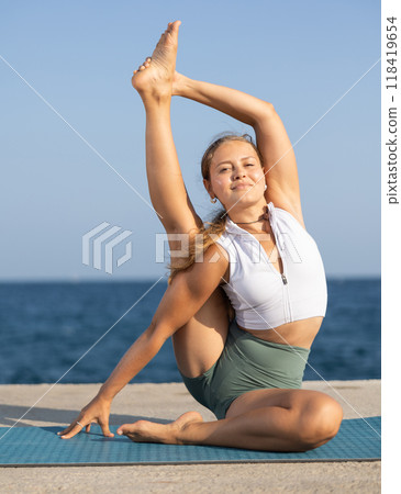 Young girl in sportwear doing stretching exercises for strong arms and abs and difficult yoga asana on the seashore on sunny day 118419654