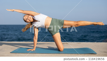 Flexible fit woman doing yoga on the seashore, performing seated back-bending asana Rajakapotasana, or King Pigeon Pose 118419656