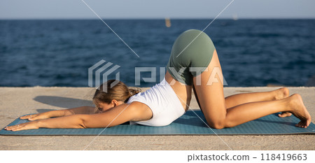 Sportive girl practicing child pose of yoga on seashore 118419663