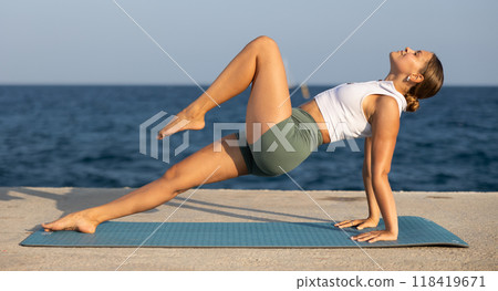 Positive girl practicing reverse plank pose of yoga on seashore 118419671