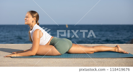 Sportive girl practicing pigeon pose of yoga on seashore Sportive girl practicing pigeon pose of yoga on seashore 118419676