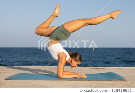 On windy day young slender woman does yoga near sea doing pincha mayurasana On windy day young slender woman does yoga near sea doing pincha mayurasana 118419691