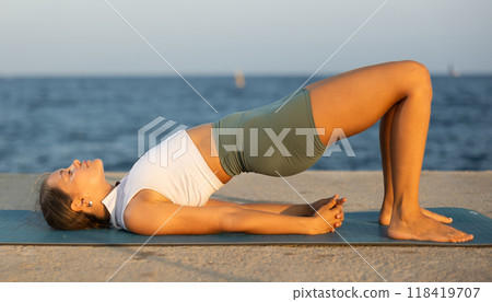 On windy day young slender woman does yoga near sea doing glute bridge On windy day young slender woman does yoga near sea doing glute bridge 118419707