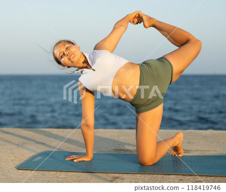 On windy day young slender woman does yoga near sea doing Crescent Moon pose On windy day young slender woman does yoga near sea doing Crescent Moon pose 118419746