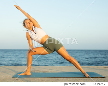 Sportive girl practicing triangle pose of yoga on seashore Sportive girl practicing triangle pose of yoga on seashore 118419747