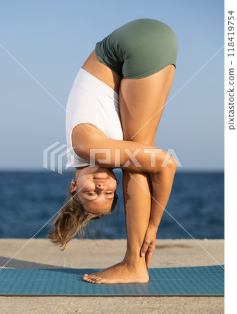 On windy day young slender woman does yoga near sea doing Parivritta Uttanasana, Uttanasana, 118419754