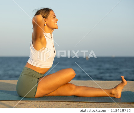 Sportive girl practicing seated yoga asana on seashore Sportive girl practicing seated yoga asana on seashore 118419755
