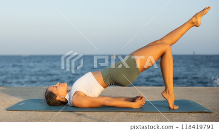 On windy day young slender woman does yoga near sea doing glute bridge On windy day young slender woman does yoga near sea doing glute bridge 118419791