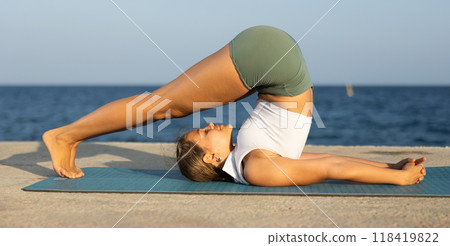 On windy day young slender woman does yoga near sea doing halasana On windy day young slender woman does yoga near sea doing halasana 118419822