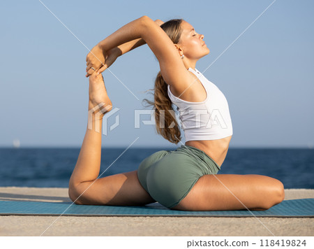 Flexible fit woman doing yoga on the seashore, performing seated back-bending asana Rajakapotasana, or King Pigeon Pose Flexible fit woman doing yoga on the seashore, performing seated back-bending asana Rajakapotasana, or King Pigeon Pose 118419824