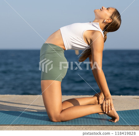 Athletic girl training camel position on mat on seashore 118419828