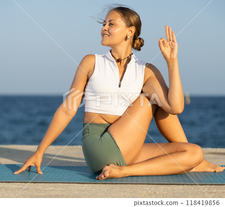 Flexible girl practicing lord of the fishes pose of yoga on seashore Flexible girl practicing lord of the fishes pose of yoga on seashore 118419856