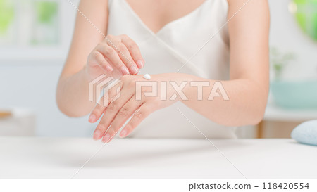 A woman applies a small amount of moisturizer to the back of her hand, showcasing a gentle skincare routine. The image exudes a fresh, minimalist feel, and personal care in bathroom background. A woman applies a small amount of moisturizer to the back of her hand, showcasing a gentle skincare routine. The image exudes a fresh, minimalist feel, and personal care in bathroom background. 118420554