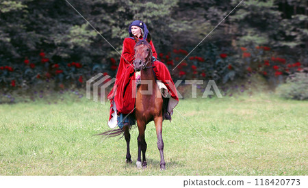BELARUS,DUDUTKI - JULY 29, 2018: MEDIEVAL FESTIVAL. Lady in a maroon opland riding a brown horse BELARUS,DUDUTKI - JULY 29, 2018: MEDIEVAL FESTIVAL. Lady in a maroon opland riding a brown horse 118420773