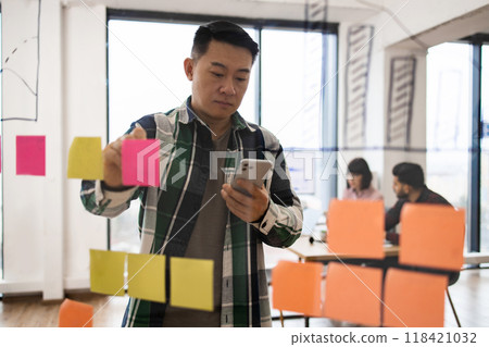 Man working with sticky notes and smartphone in office 118421032