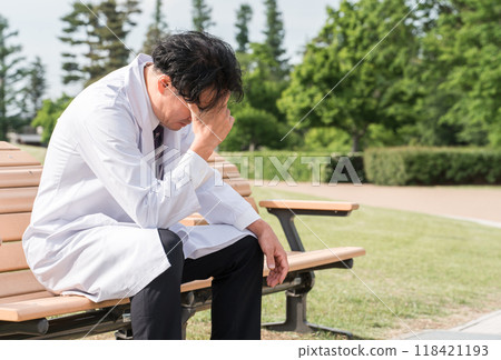 一位男醫生在公園的長椅上感到沮喪(擔憂、遺憾、思考、痛苦) 一位男醫生在公園的長椅上感到沮喪(擔憂、遺憾、思考、痛苦) 118421193