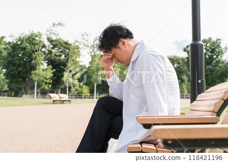 A male doctor feeling down on a park bench (worried, regretful, thinking, suffering) 118421196
