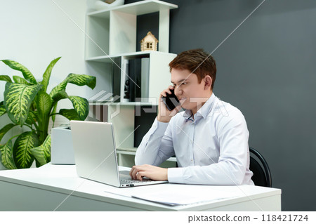 focused young man is actively discussing a project over the phone while working at a computer in a modern office environment focused young man is actively discussing a project over the phone while working at a computer in a modern office environment 118421724