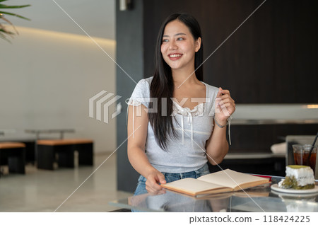 A woman sitting in a coffee shop, looking out the window for inspiration while writing in her book. A woman sitting in a coffee shop, looking out the window for inspiration while writing in her book. 118424225