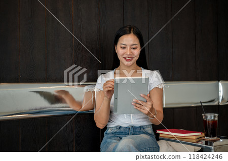 A beautiful Asian woman using a digital tablet, working remotely from a coffee shop. A beautiful Asian woman using a digital tablet, working remotely from a coffee shop. 118424246