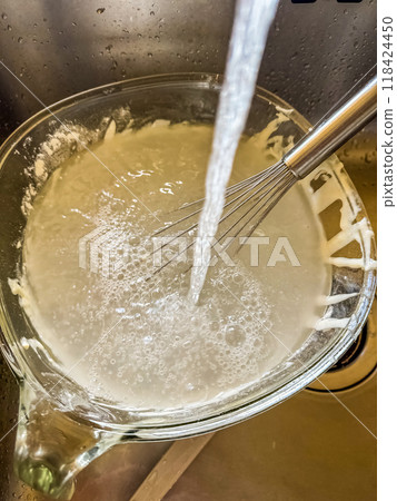 Used glass bowl after making pancake batter under water with mixer in sink . High quality photo 118424450