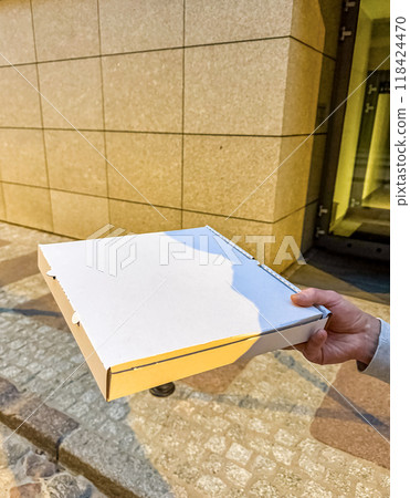A person holding a white cardboard pizza box, captured outdoor in front of wall. High quality photo A person holding a white cardboard pizza box, captured outdoor in front of wall. High quality photo 118424470